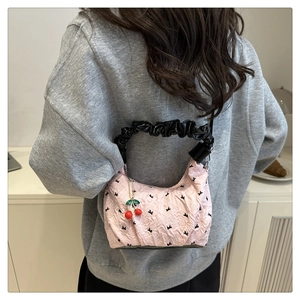 Detail of pink quilted dumpling bag featuring black floral patterns and cherry charm