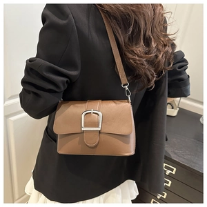 Detailed close-up of a brown leather shoulder bag with a silver buckle on a model