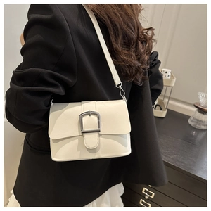 Detail view of a white patent leather shoulder bag with a large silver buckle on a model