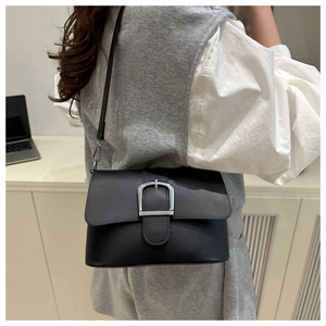 Detail of a black patent leather shoulder bag with a silver U-shaped metal clasp