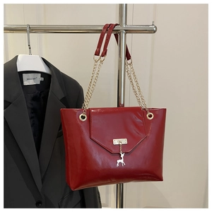 Detail of red glossy tote bag featuring a silver deer charm and gold chain strap