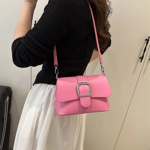 Pink patent leather crossbody bag with silver buckle worn by a model in casual style