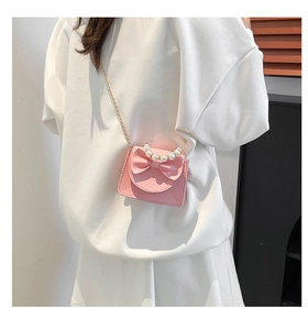 Pink mini crossbody bag with pearl handle and bow detail worn by a model