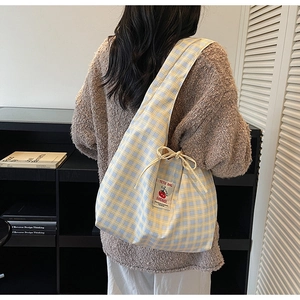 Detail of checkered tote bag with drawstring closure and cartoon tomato brand patch