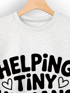 Detail of grey crewneck sweatshirt featuring Helping Tiny Humans text and heart print