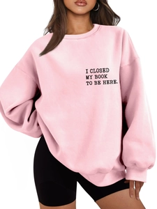 Detail of light pink sweatshirt with 'I CLOSED MY BOOK TO BE HERE' black text print