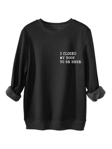 Detail of white serif text 'I CLOSED MY BOOK TO BE HERE' on black thick sweatshirt