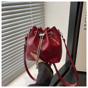 Detail of red glossy bucket bag with drawstring closure, silver chain and pearl charm