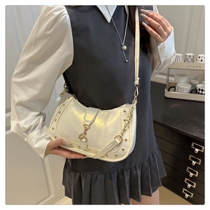Detail view of white crescent bag with gold studs and metal hook buckle on strap
