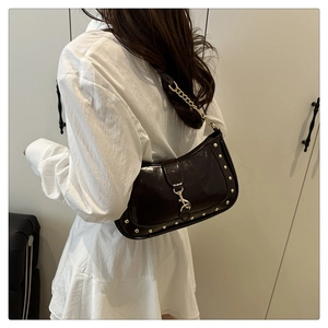 Detail of dark patent leather underarm bag with gold studs and metal hook buckle