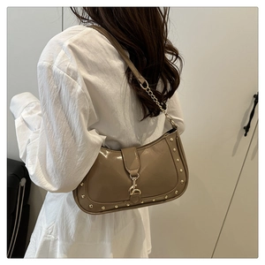 Close-up of brown crescent bag with gold rivets and chain strap on a white dress model