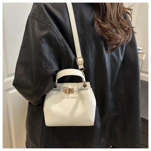 Détail du sac seau en cuir grainé blanc avec fermoir rotatif doré sur une veste en cuir noir