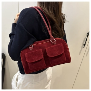 Close-up of a burgundy suede shoulder bag with dual front flap pockets on a model