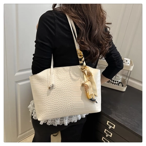 Detail of white crocodile embossed tote bag with elegant golden silk scarf handle decor