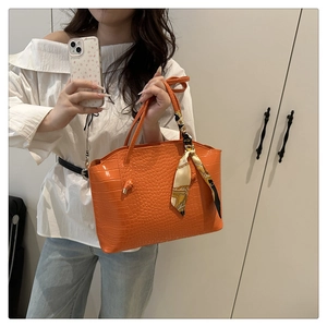 Close-up of bright orange crocodile embossed tote bag with decorative floral silk scarf