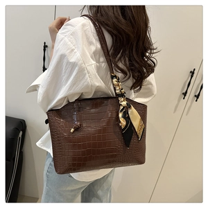 Detail of dark brown crocodile embossed leather handbag with chic decorative silk scarf