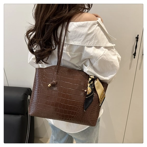 Detail of dark brown crocodile-embossed tote bag with a silk scarf handle accessory