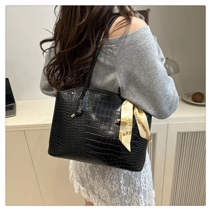Macro shot of black crocodile embossed leather tote bag featuring elegant silk scarf detail