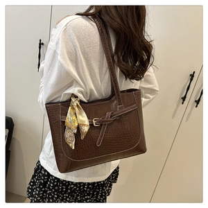 Detail of dark brown croc-embossed tote bag with decorative silk scarf on shoulder