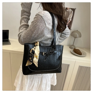 Detail of black crocodile texture tote bag with white stitching and decorative silk scarf