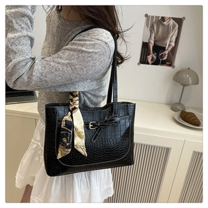 Close-up of black crocodile pattern tote bag with decorative metal buckle and silk scarf