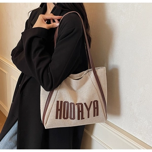 Close-up of durable canvas tote bag featuring HOORYA lettering and sturdy brown handles