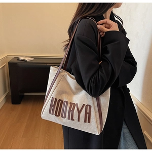 Detail of canvas tote bag with brown leather handles and HOORYA embroidery worn on shoulder