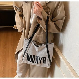 Detail of canvas tote bag showing black leather straps and printed HOORYA text