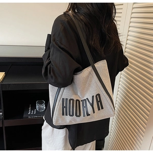 Detailed side view of grey canvas tote bag with black leather straps and lettering