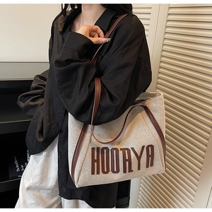 Detail of canvas tote bag with brown leather trim and embroidered HOORYA lettering