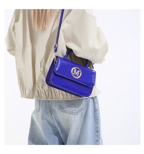 Dettaglio della borsa in pelle verniciata blu con logo M dorato sulla modella