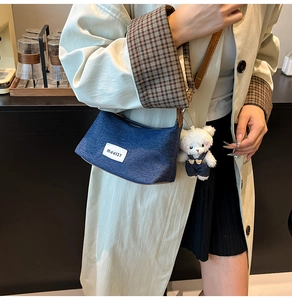 Detail of dark blue denim handbag featuring a white brand tag and a plush bear pendant