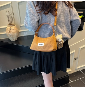 Detail of mustard yellow corduroy handbag featuring a bear charm and leather straps