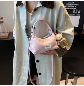 Detailed texture of pink corduroy shoulder bag with bear pendant worn by model