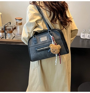 Detail of retro black leather tote bag with a cute plush bear charm and ribbon accent