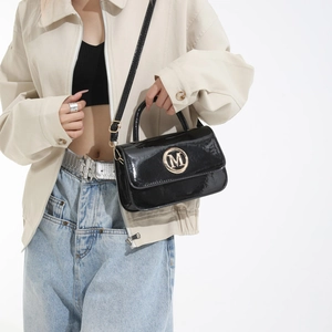 Modern black patent leather handbag with gold M logo shown at a 45-degree angle