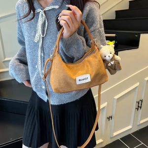 Brown suede crescent bag with a cute teddy bear charm, styled on a minimalist indoor staircase