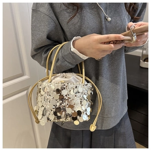 Detailed close-up of shiny silver sequins and golden metal handles on drawstring bucket bag