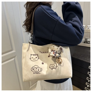 Detail of beige tote bag with cat illustration and cute plush charm on a shoulder strap