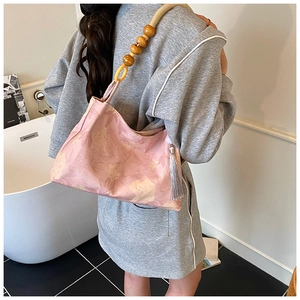 Détail du sac seau floral avec bandoulière en perles de bois et pompons en soie élégants