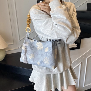 Sac seau bleu à fleurs avec poignée en perles de bois et gland, porté par un modèle