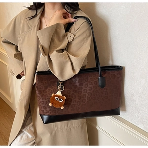 Detail of leopard print tote bag featuring a plush monster charm and black leather straps