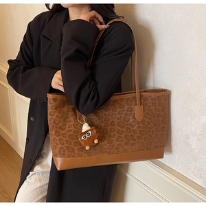 Close-up of leopard print tote bag with brown leather handles and plush monster charm