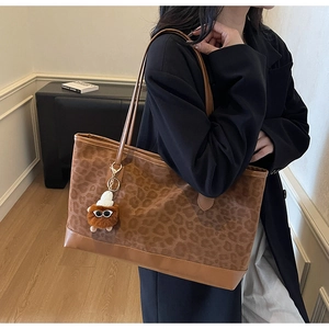 Detail view of large leopard print tote bag with plush doll charm and brown leather base