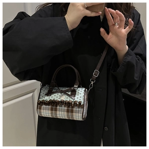 Détail du sac à main bleu à carreaux avec nœud, porté par un mannequin en manteau noir