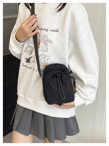 Détail du sac bandoulière en nylon noir avec cordon et étiquette orange latérale