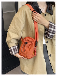 Détail du sac bandoulière orange en nylon avec cordon et broderie lettrage