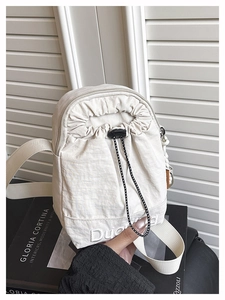 Detalle del bolso bandolera crema con cordón ajustable, logo y bolsillo con cremallera