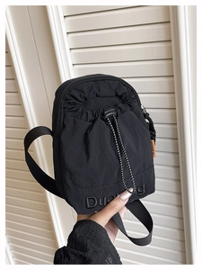 Détail du sac bandoulière en nylon noir avec étiquette orange et lettrage brodé