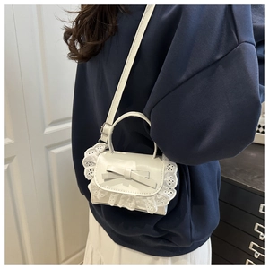 Chic white mini crossbody bag with bow detail and lace trim shown on a model